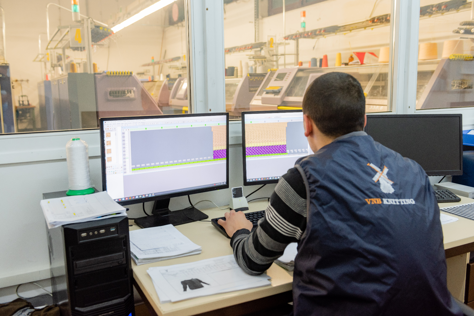 VNB Knitting programmer at workstation with Stoll machines in background